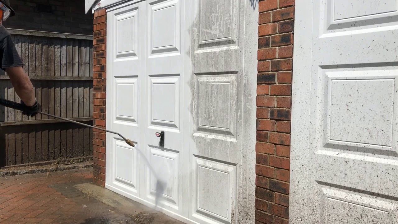 A person is cleaning a garage door with a high pressure washer.