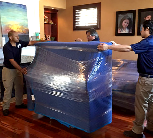 A group of men are wrapping a piano in plastic wrap.