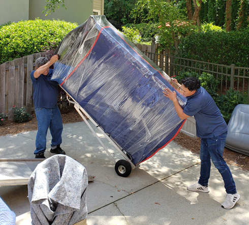 Two men are carrying a large blue box on a cart.