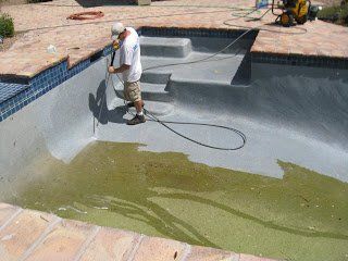 A man is cleaning a swimming pool with a vacuum cleaner.