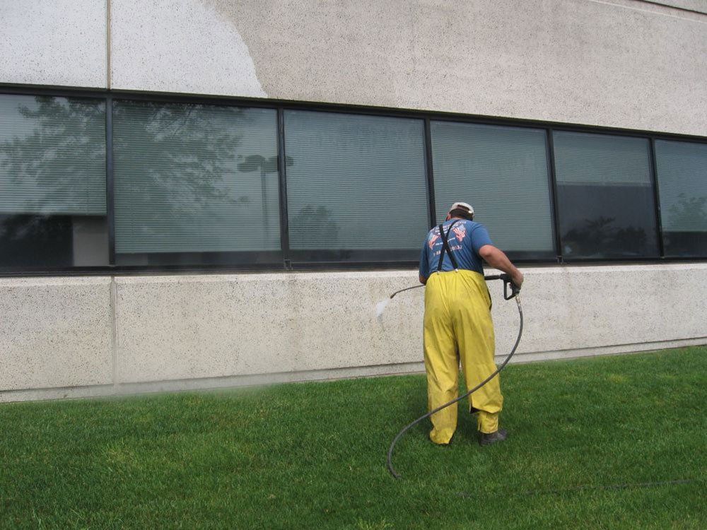 A man in yellow overalls is cleaning the side of a building