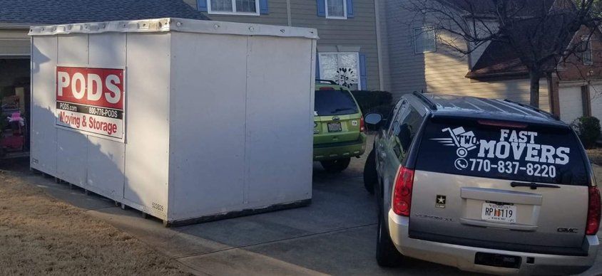Two cars are parked in front of a house next to a pods storage container.