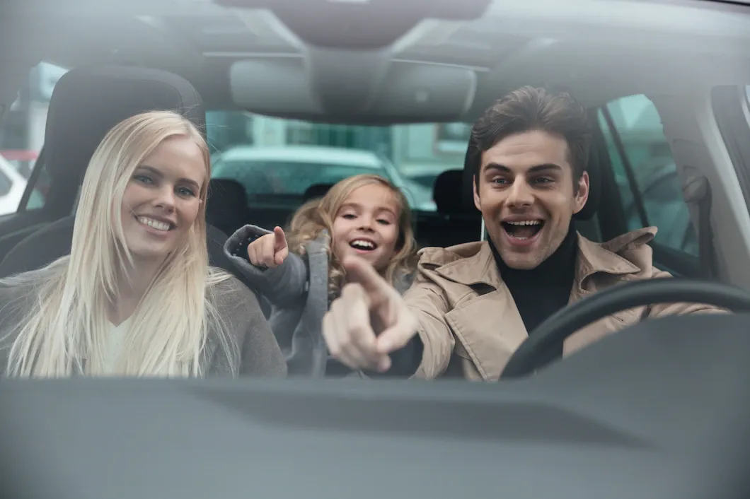 A family is sitting in a car and pointing at the camera.