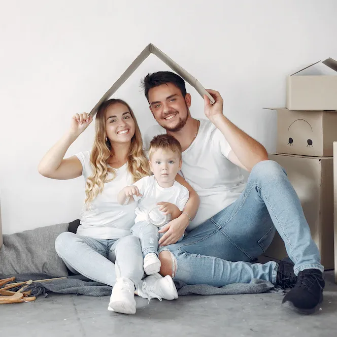 A family is sitting on the floor holding a cardboard house.