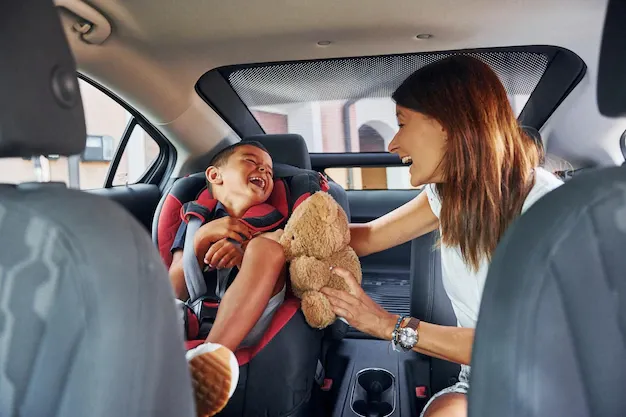 A woman is putting a child in a car seat.
