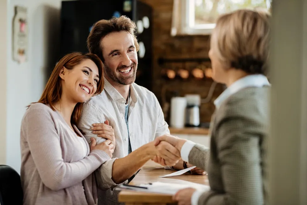 A man and woman are shaking hands with a woman while sitting at a table.