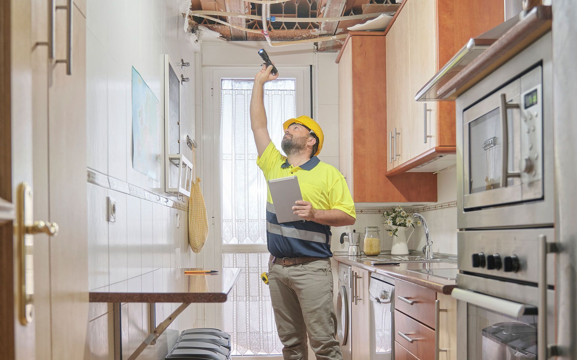 Man in hard hat inspects water-damaged kitchen ceiling.