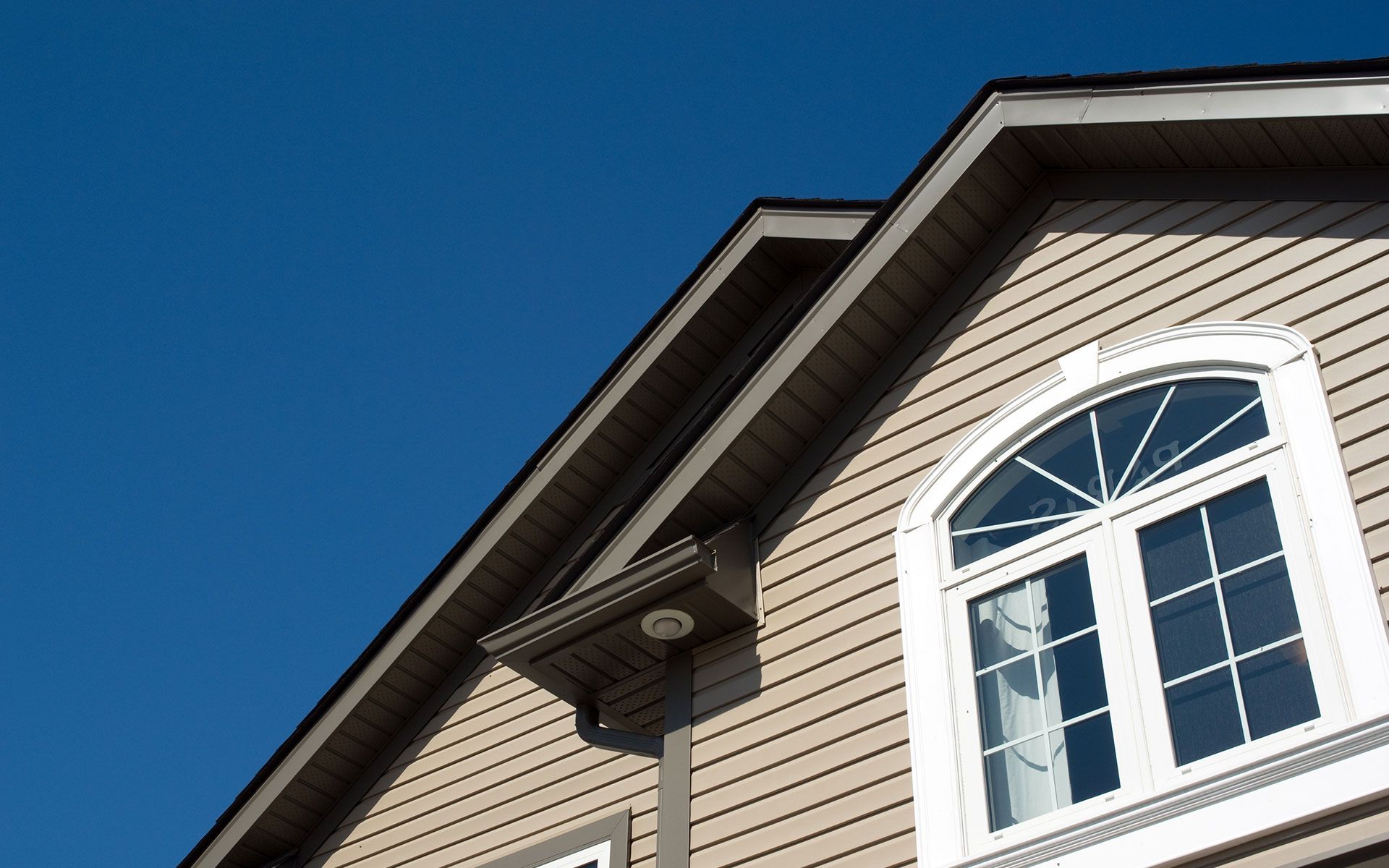 Tan house exterior with a white-framed arched window against a clear blue sky.