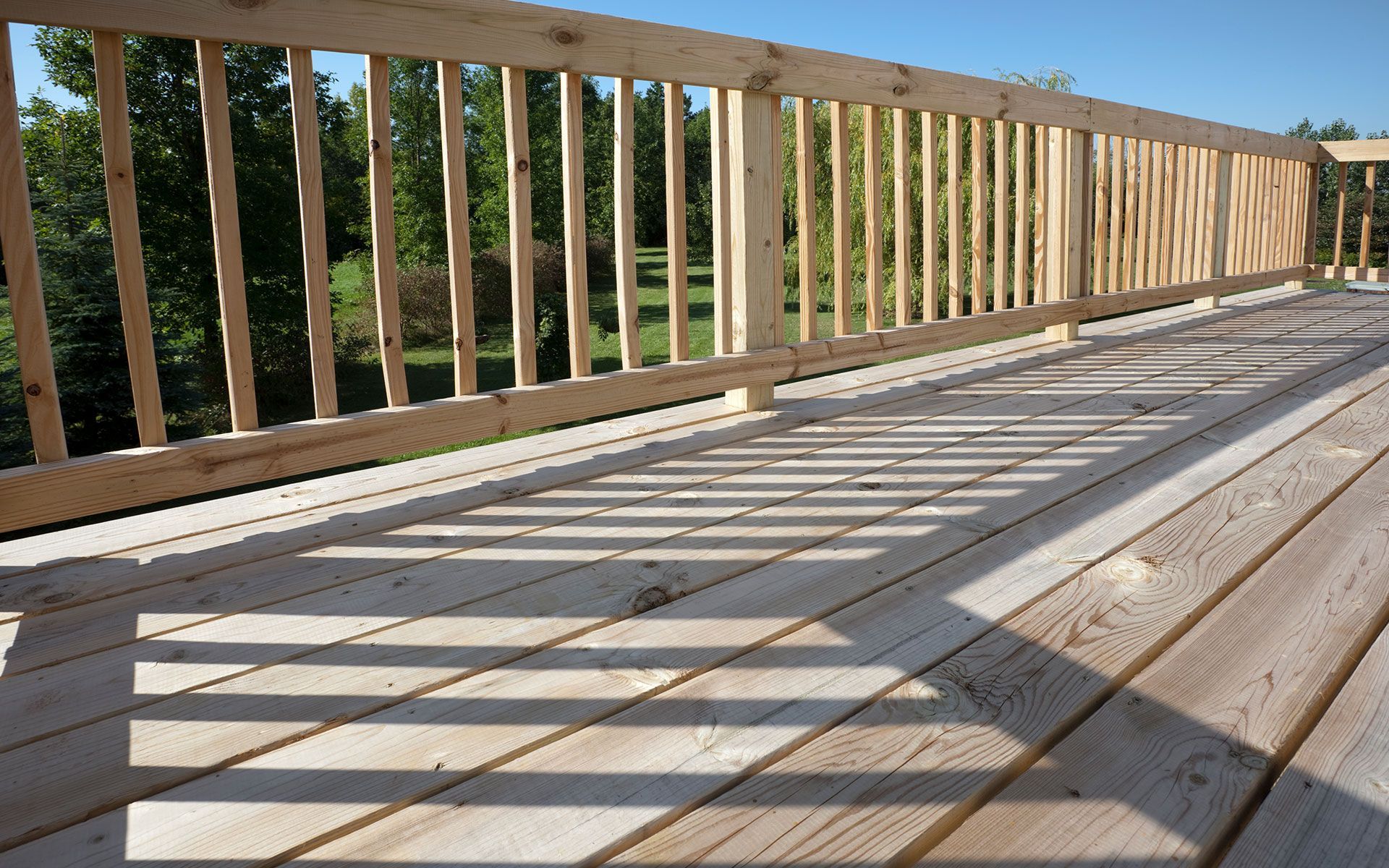 Wooden deck with railing, casting shadows in sunlight.