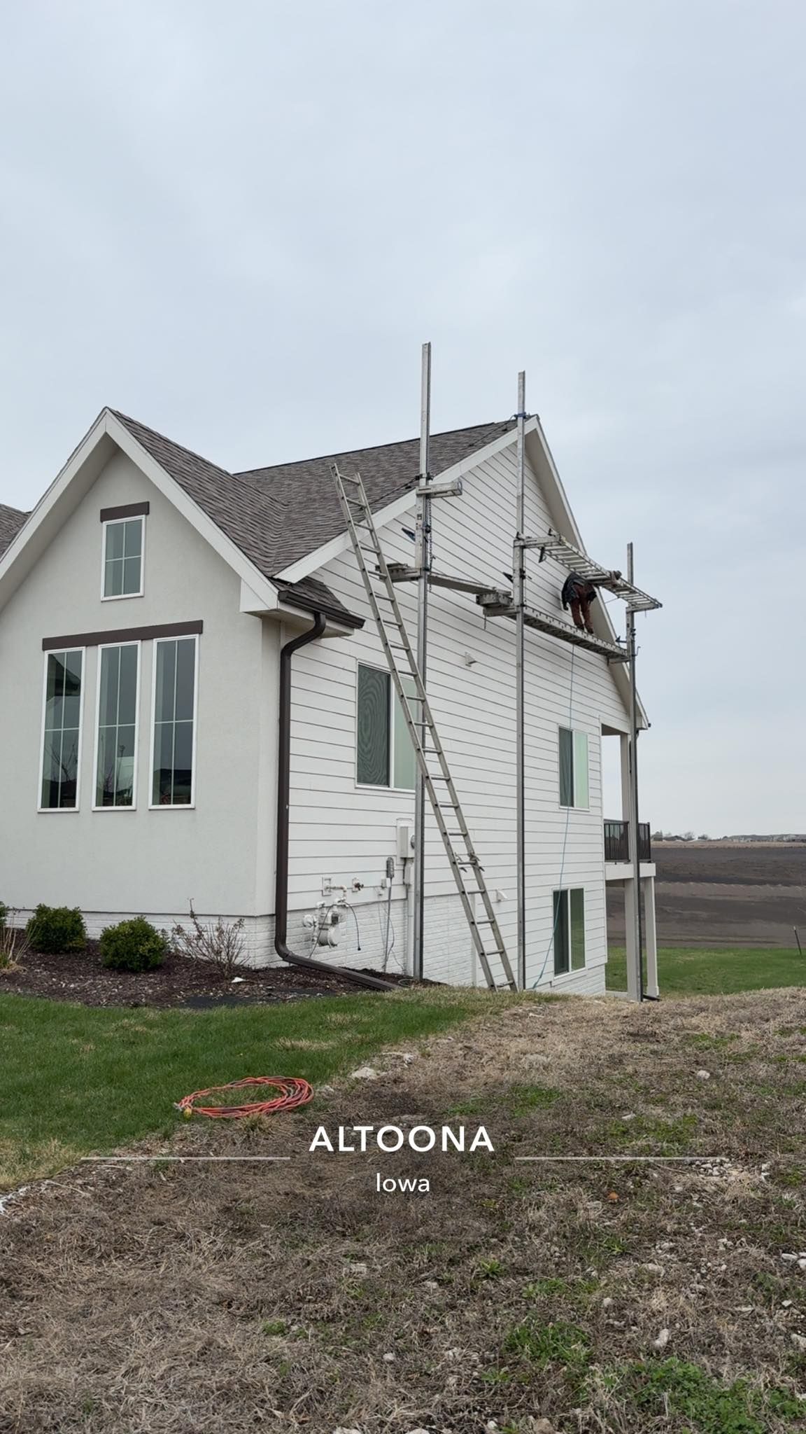 Construction worker in safety gear on a ladder, inspecting a roof, taking notes.