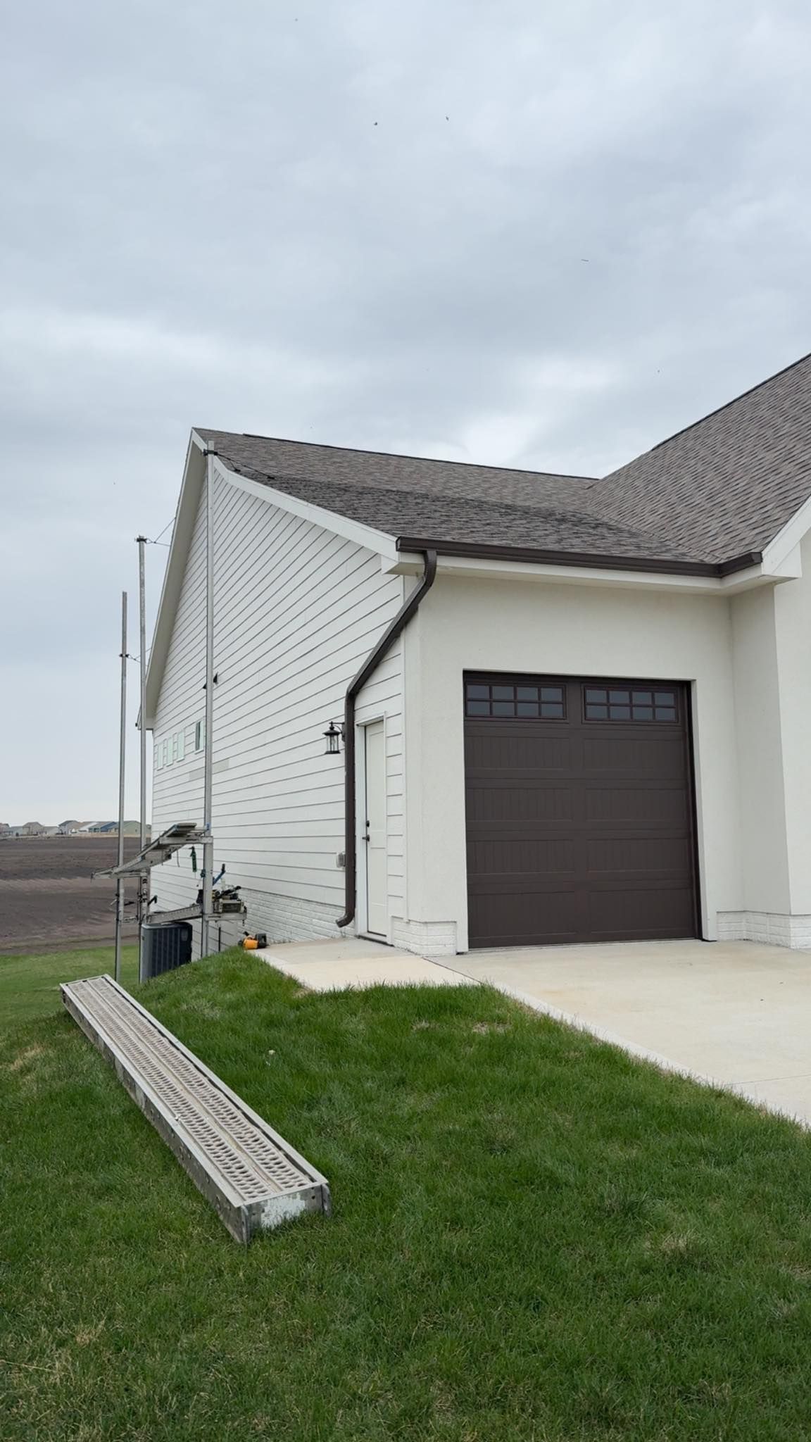 Man in plaid shirt repairs siding on a house. He's kneeling with tools near the exterior wall.