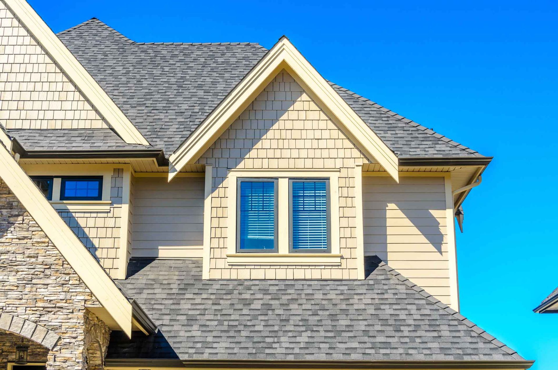 Cream-colored house exterior with gray shingles and blue-trimmed windows under a clear blue sky