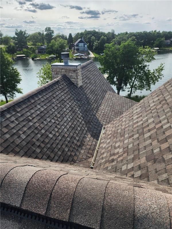 Roofer hammers copper flashing onto a shingled roof, wearing gloves.