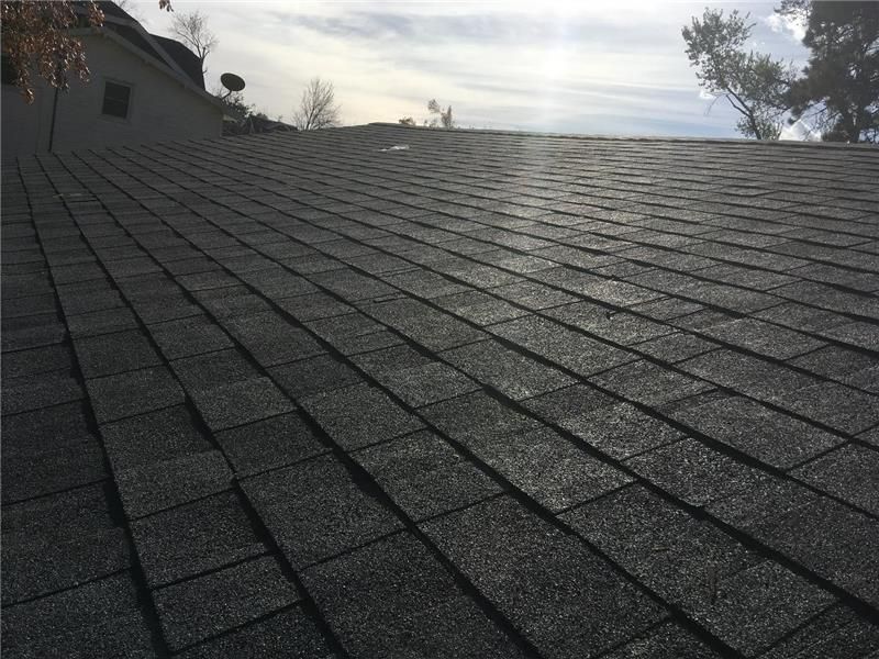 Roofer hammers copper flashing onto a shingled roof, wearing gloves.