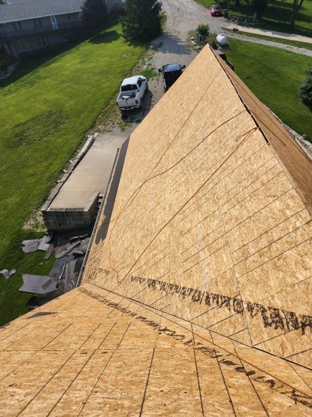 Aerial view of roofing job with exposed roof deck and discarded shingles on ground.