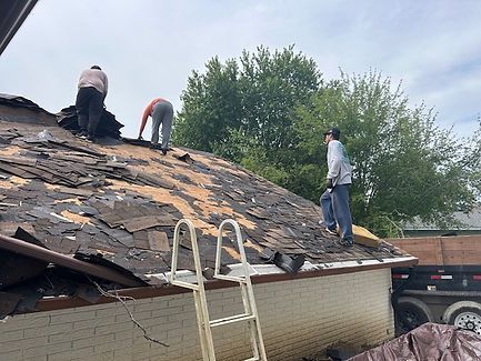 Three people removing shingles from a roof. A ladder is present.