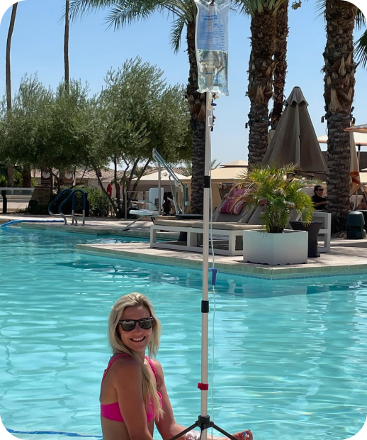 A woman in a pink bikini is sitting in a swimming pool doing iv therapy
