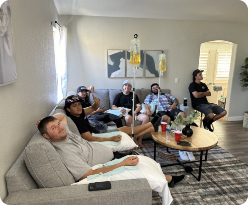 A group of men are sitting on a couch in a living room doing iv therapy