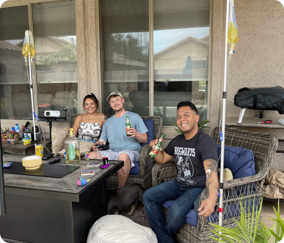 A group of people are sitting on a patio holding bottles of beer doing iv therapy