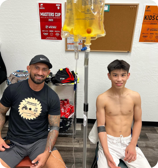 A man and a boy are sitting in front of a masters cup sign doing iv therapy
