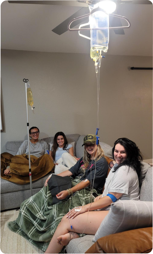 A group of people are sitting on a couch with iv drips hanging from the ceiling.