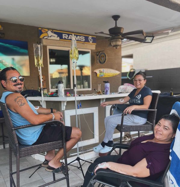 Group of friends socializing outdoors, two receiving IV hydration therapy.