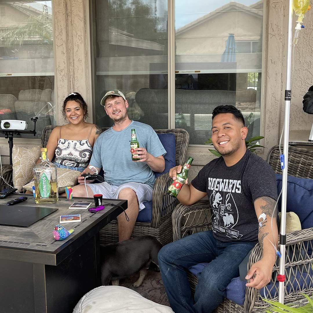 Group of friends socializing outdoors, two receiving IV hydration therapy.