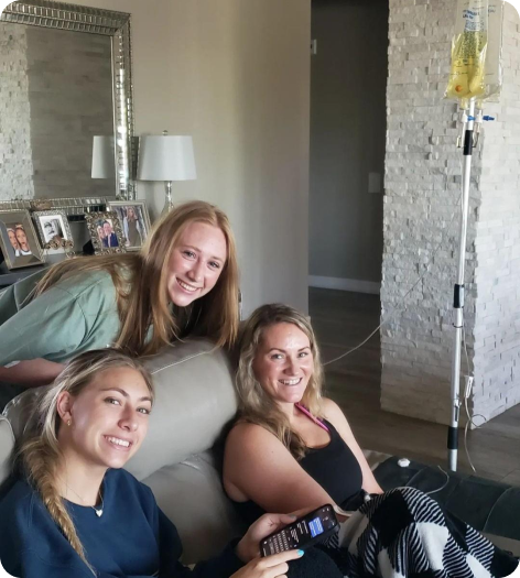 Three women are sitting on a couch in a living room doing iv therapy