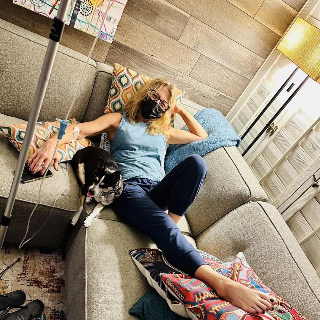 Woman relaxing on a sofa with IV therapy and her dog beside her at home