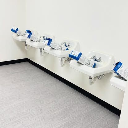 Row of white sinks with blue boxes in a room with gray floor and white walls.