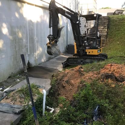 Mini excavator digging near a concrete wall and steps, in a grassy area.