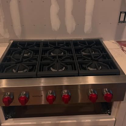 Stainless steel Wolf range with six red knobs and black burner grates.
