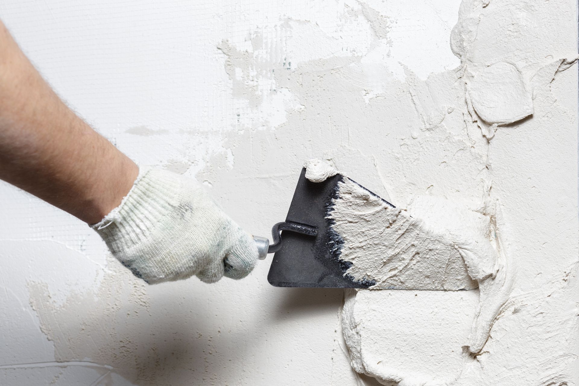 Worker applying gypsum compound to repair stucco on a wall using a spatula.