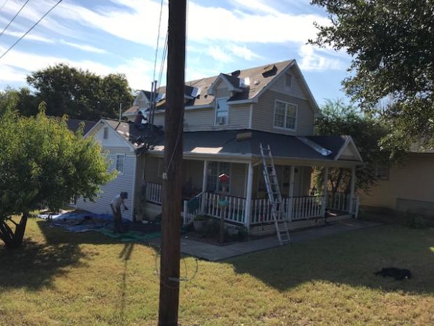 Two-story house with roofers, ladders, and debris. Porch in front. Sunny day.