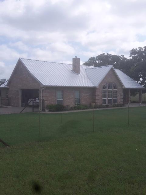 Brick house with a metal roof on a grassy field under a cloudy sky.