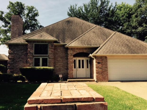 Brick house with a white door, garage, and dark roof. Brick path in front, trees in the background.