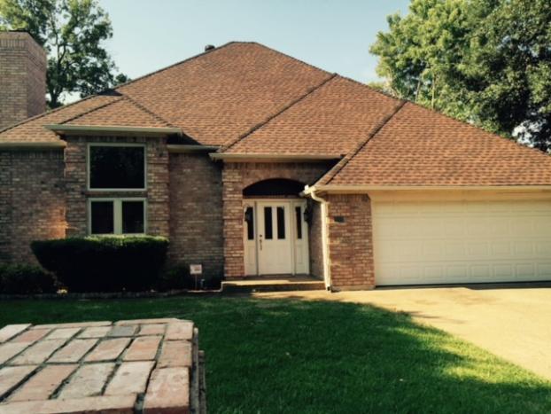 Brick house with brown roof, white garage door, and front door with arched entrance.
