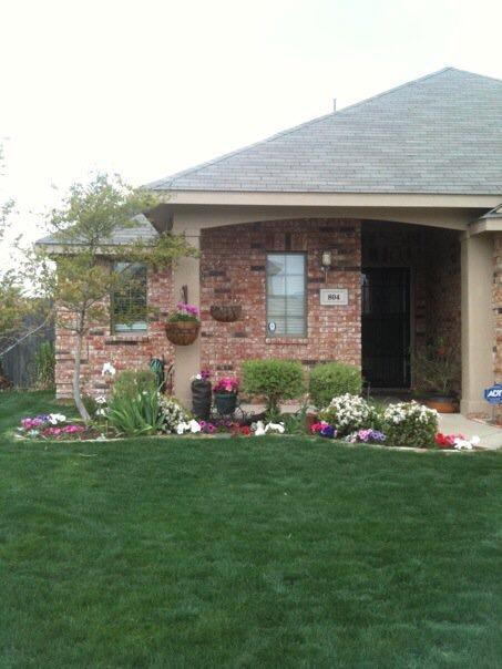 Brick house with flower beds, green lawn, and overcast sky.