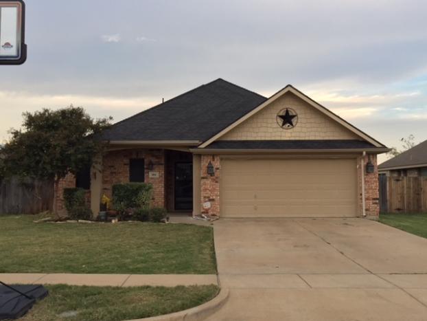 Single-story brick house with beige garage door, brown roof, and a star decoration under the roof peak.