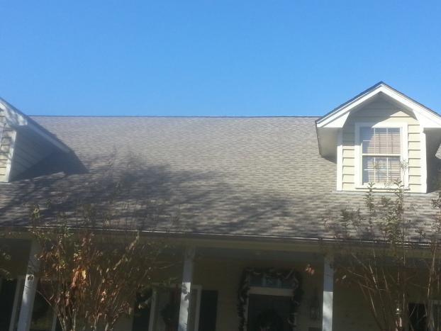 A house with a gray shingle roof, two dormers, and a porch against a blue sky.