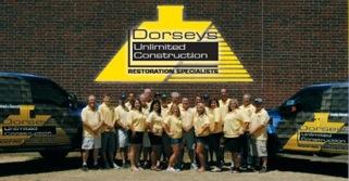 Group of people in yellow shirts in front of brick wall and Dorsey's Unlimited Construction vehicles.
