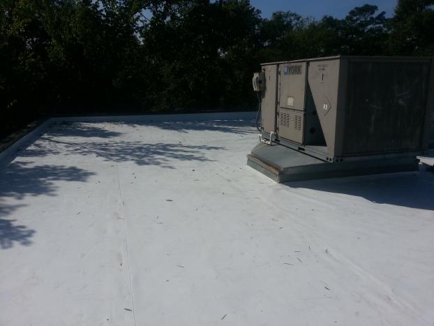 White flat roof with HVAC unit, trees in the background on a sunny day.