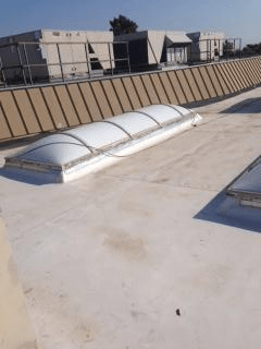 White skylight on a flat, white commercial roof with HVAC units in the background.