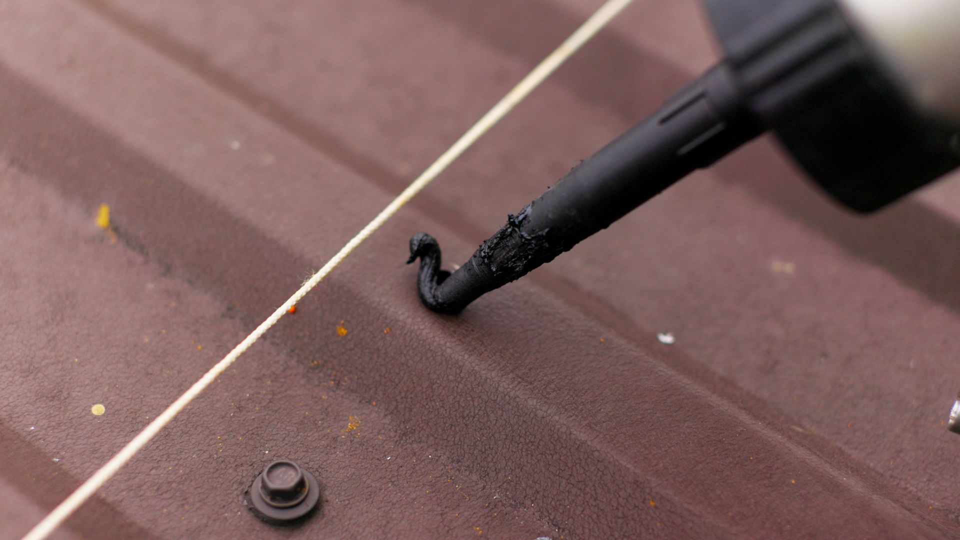 Close-up of applying black sealant on a brown metal roof seam using a caulking gun nozzle Close-up of applying black sealant on a brown metal roof seam using a caulking gun nozzle