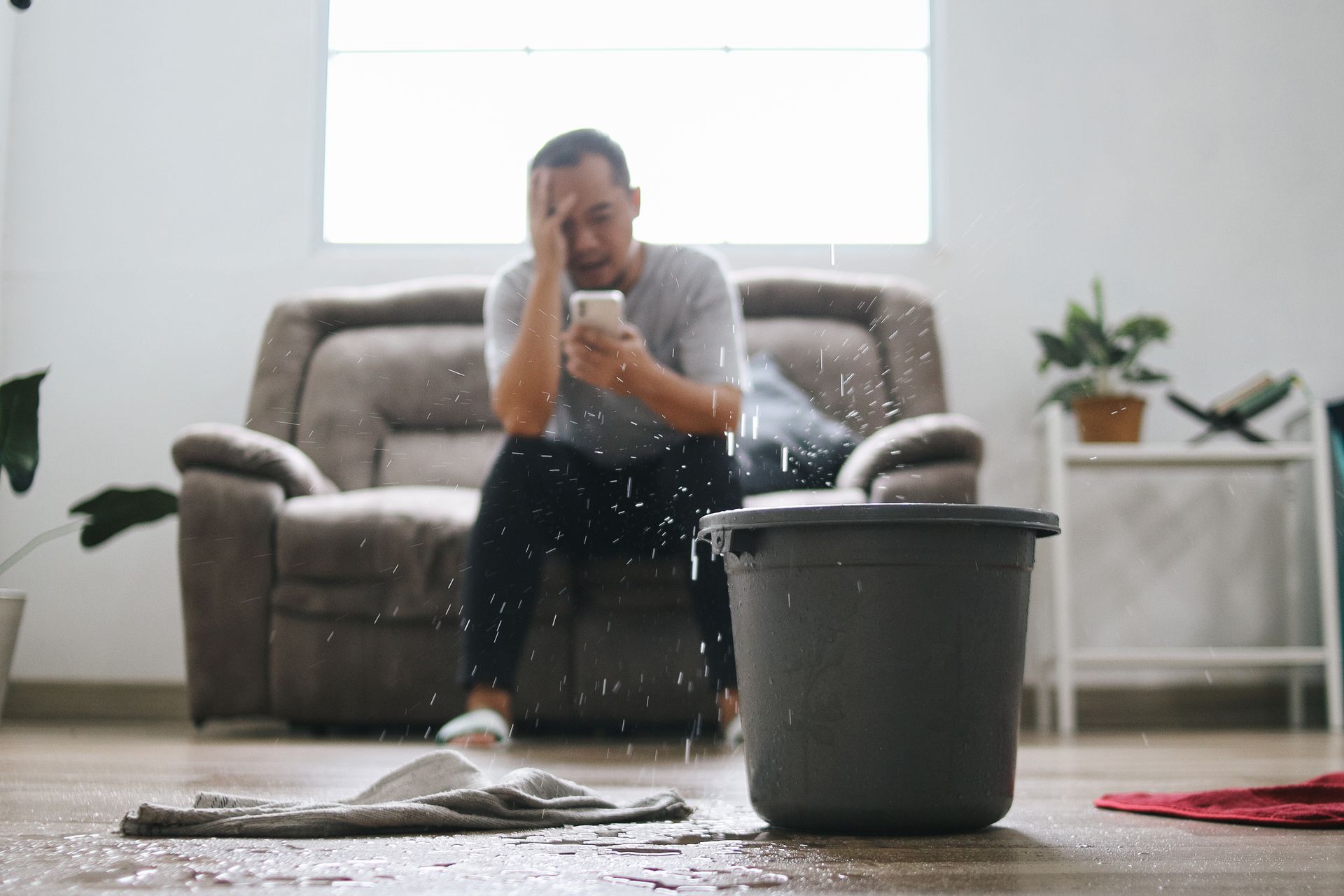 Stressed man calling for repair of roof leak at home. Put a bucket for water for the leaks.