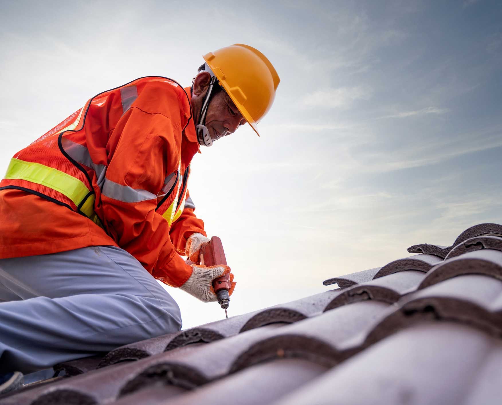 Roof replacement contractor installing tiles on a new roof using an electric drill.
