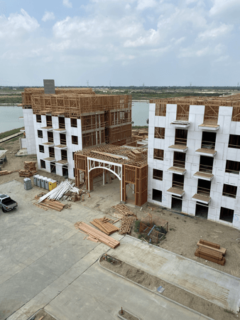 Construction site with wooden frames of multi-story buildings, gray and white exterior, cloudy sky.
