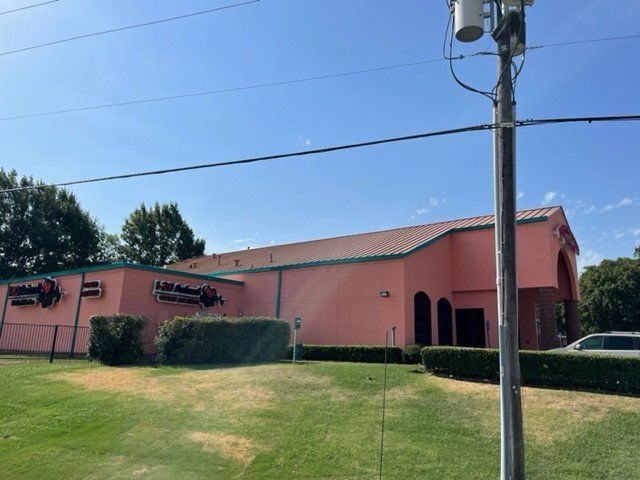 Pink building with a red roof and signs for a restaurant on a green lawn. Bright sunny day.