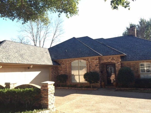 Brick house with dark roof, arched doorway, and attached garage.