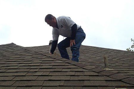 Man on a roof inspecting shingles. Cloudy sky overhead.